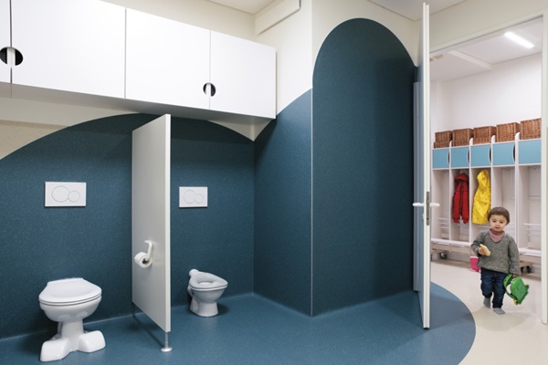 Concept de salle de bains dans une crèche : le revêtement de sol se fond dans la décoration murale.